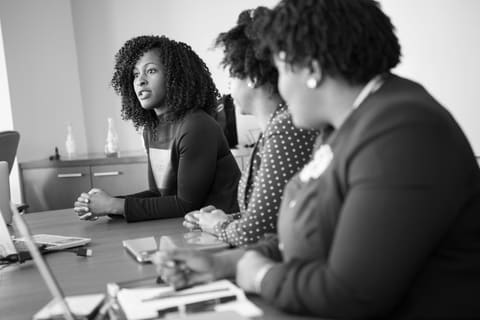 Three professional women in discussion around a meeting table