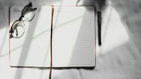 An open notebook with a pen and glasses on a desk